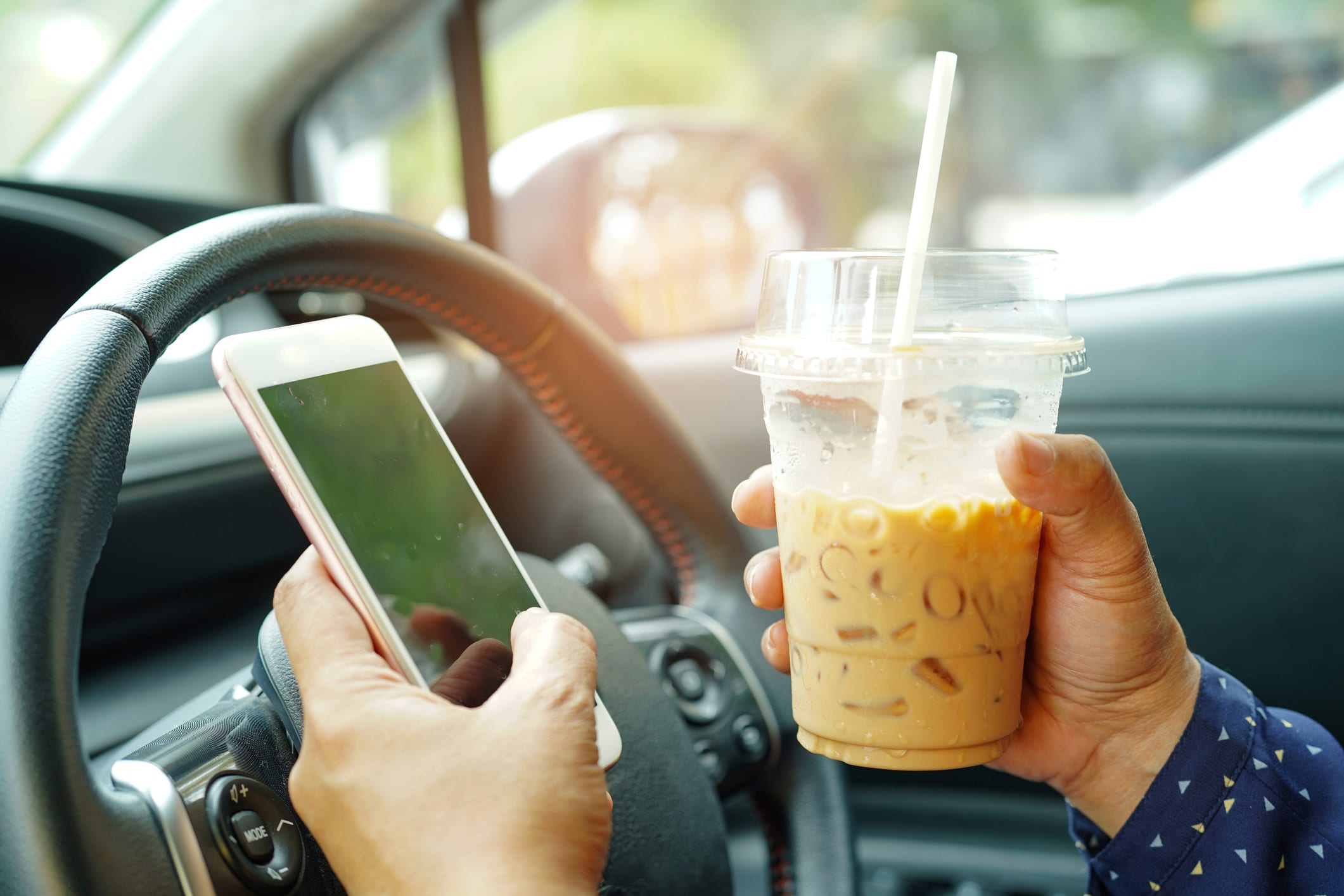 A driver holds their cell phone and a coffee instead of the wheel.